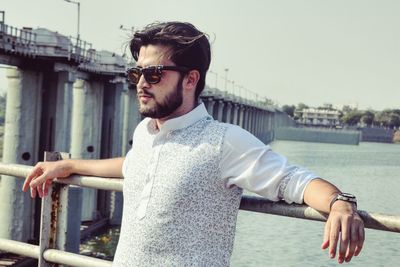 Man in sunglasses standing against lake and sky