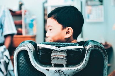 Rear view of smiling boy sitting on chair at barber shop