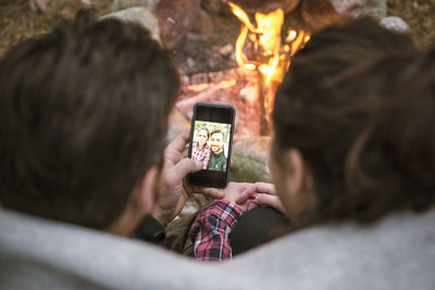 High angle view of couple taking selfie in mobile phone by fire pit at campsite