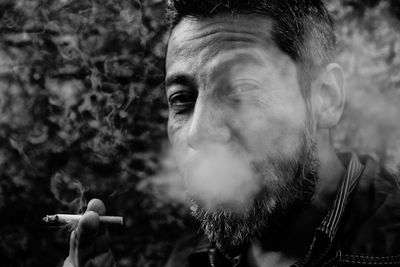 Close-up portrait of man smoking while sitting against plants