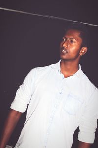 Young man looking away while standing against black background