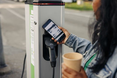 Woman using app on smart phone near kiosk at charging station