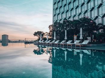 Buildings by swimming pool against sky during sunset