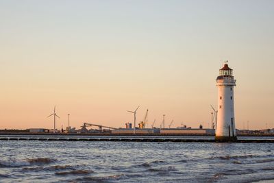 Lighthouse by sea against sky during sunset