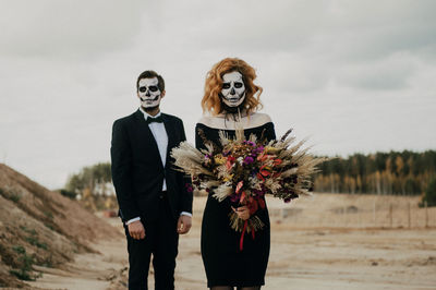 A couple in love celebrates halloween in costumes and makeup with a bouquet of dried flowers