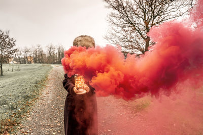 Beautiful middle aged woman on a country road showing a lantern that releases red smoke