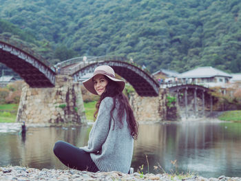 Woman sitting by lake against trees