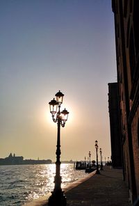 Silhouette street light by sea against clear sky