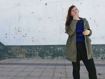 Full length of young woman standing against wall