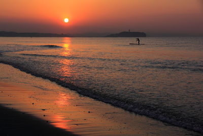 Person paddleboarding in sea against sky during sunset