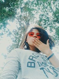 Low angle portrait of young woman wearing sunglasses at park