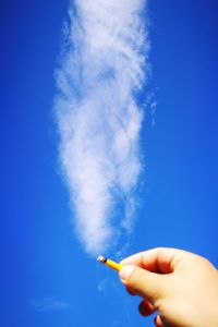 Close-up of hand holding cigarette against blue sky