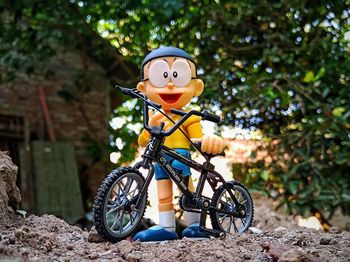 Bicycle toy on rock by tree