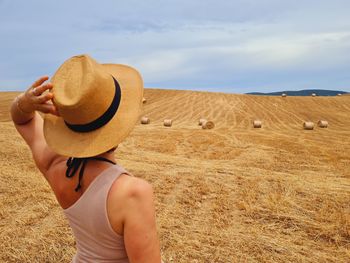 Woman from behind with hat walks in a harvested wheat field