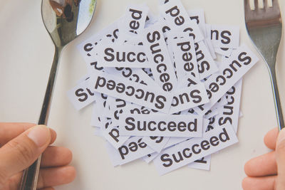 Cropped hands of woman holding fork and spoon by plate with papers