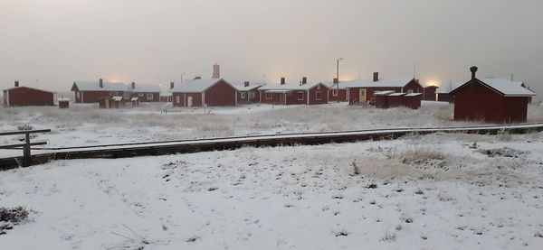 Snow covered houses on field by buildings against sky