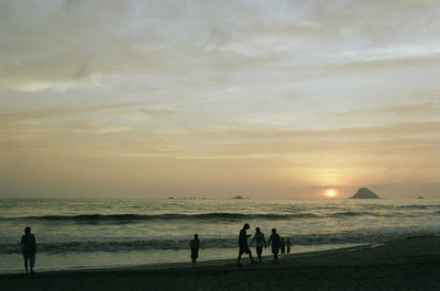 Silhouette people standing on beach against sky during sunset