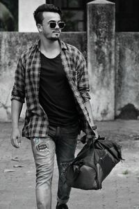 Young man wearing sunglasses while walking with luggage