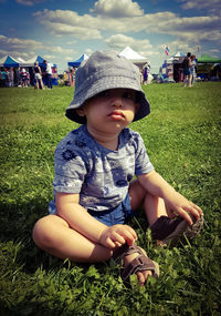 Portrait of boy wearing bucket hat while sitting on grassy field