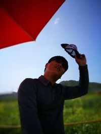 Midsection of man holding red umbrella against sky