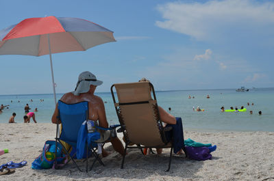 Rear view of people sitting on chair at beach