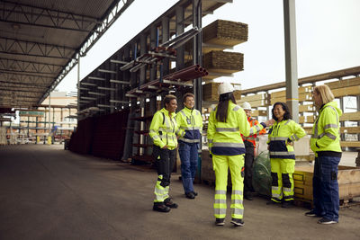 Female engineer discussing with multiracial colleagues while standing at lumber industry