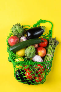 Textile mesh bag with produce, fruits and vegetables on yellow background. zero waste, eco-friendly