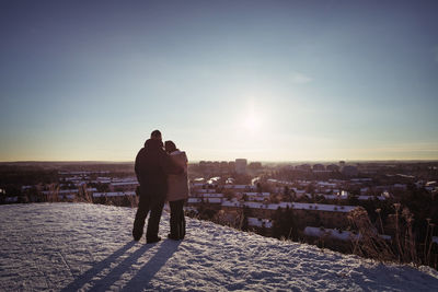 Full length rear view of couple embracing while standing on mountain during winter