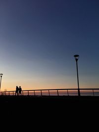 Silhouette people walking on bridge against sky during sunset