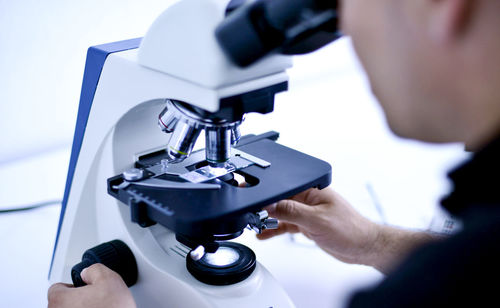 Midsection of male scientist looking through microscope at laboratory