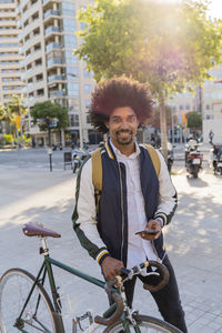 Portrait of smiling casual businessman with bicycle and cell phone in the city, barcelona, spain