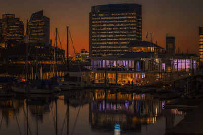 Illuminated harbor by sea against sky at dusk