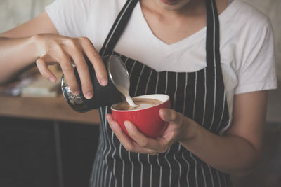 Midsection of woman pouring milk in coffee cup