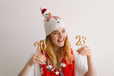 Funny young girl in a new year's hat and red scarf holds the numbers 2023 in her hands.