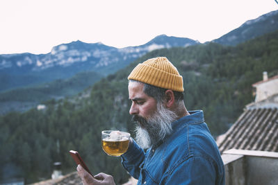 Man on his smartphone with a cup of coffee in the mountains. independent man. remote work