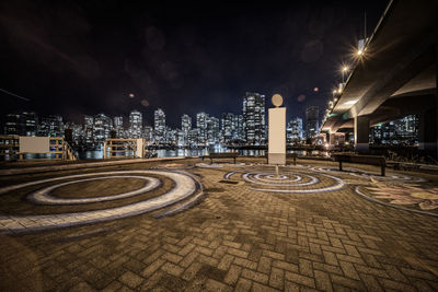 Illuminated street amidst buildings against sky at night