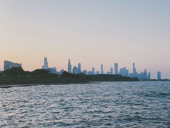 Sea by buildings against clear sky during sunset