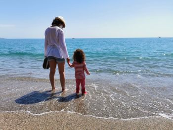 Mother and daughter hand in hand with bare feet in front of the beach with copy space.
