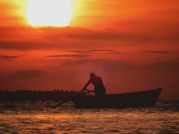 Silhouette man on boat in sea against orange sky