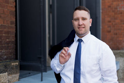 Portrait of young businessman smiling while standing against built structure