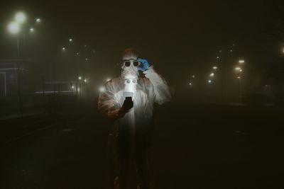 Portrait of young man wearing protective suit holding smart phone standing outdoors