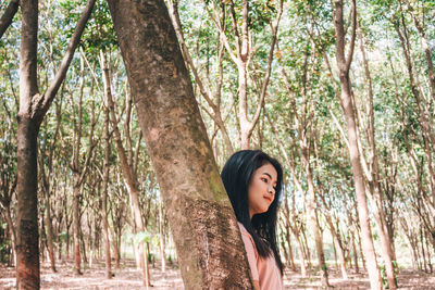 Thoughtful young woman with long hair standing by tree in forest