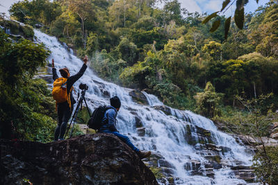 Rear view of friends photographing waterfall in forest