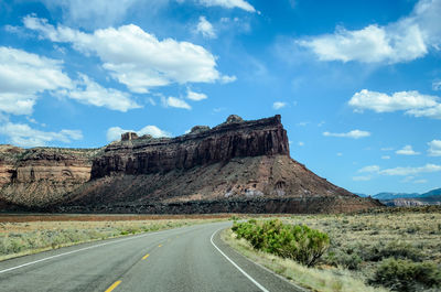 Road leading towards rocky mountains against sky