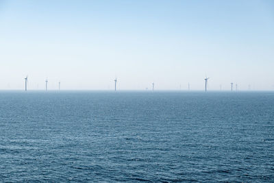 A cluster of turbines of a wind farm on the blue glittering sea under a cloudless blue sky