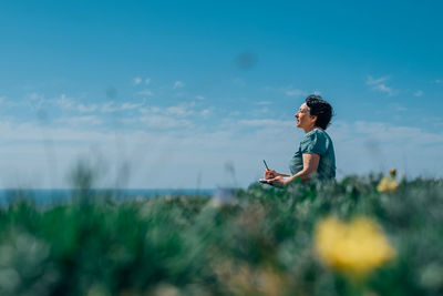 Adult woman thoughtfully writes plans diary on a sunny day on a mountain against backdrop of the sea