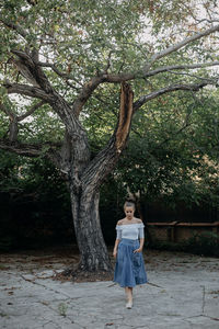 Full length of woman walking on footpath against tree