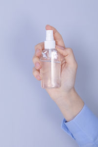 Close-up of hand holding bottle against blue background