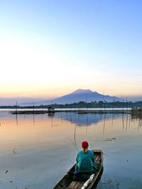 Rear view of woman in boat on calm lake against sky