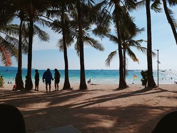 People by palm trees on beach against sky